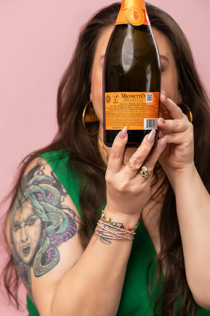 Woman holding a bottle of vegan Mionetto prosecco covering face, blog about whether alcohol is vegan and hidden animal ingredients
