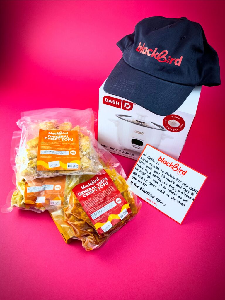 Blackbird Foods Crispy Tofu products displayed with a Blackbird hat, rice cooker, and handwritten note on a bright pink background.