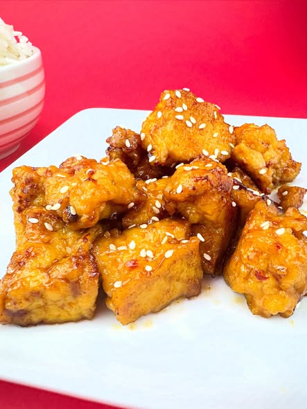Close-up of Blackbird Foods General Tso's Crispy Tofu coated in orange sauce and topped with sesame seeds.