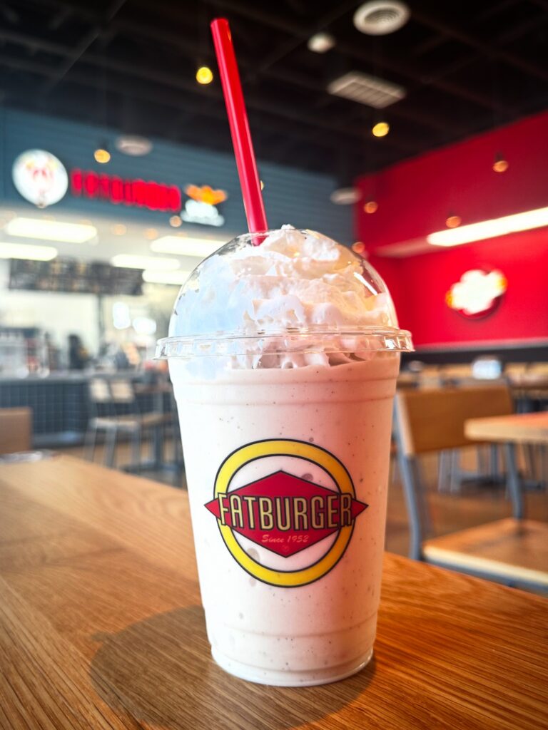 Close-up of a Fatburger vegan banana milkshake topped with dairy-free whipped topping in a dine-in restaurant setting.