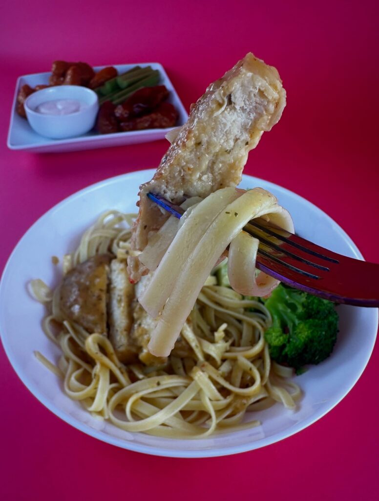 Close-up of sliced MorningStar Farms Chik'n Breast lifted with a fork over pasta.