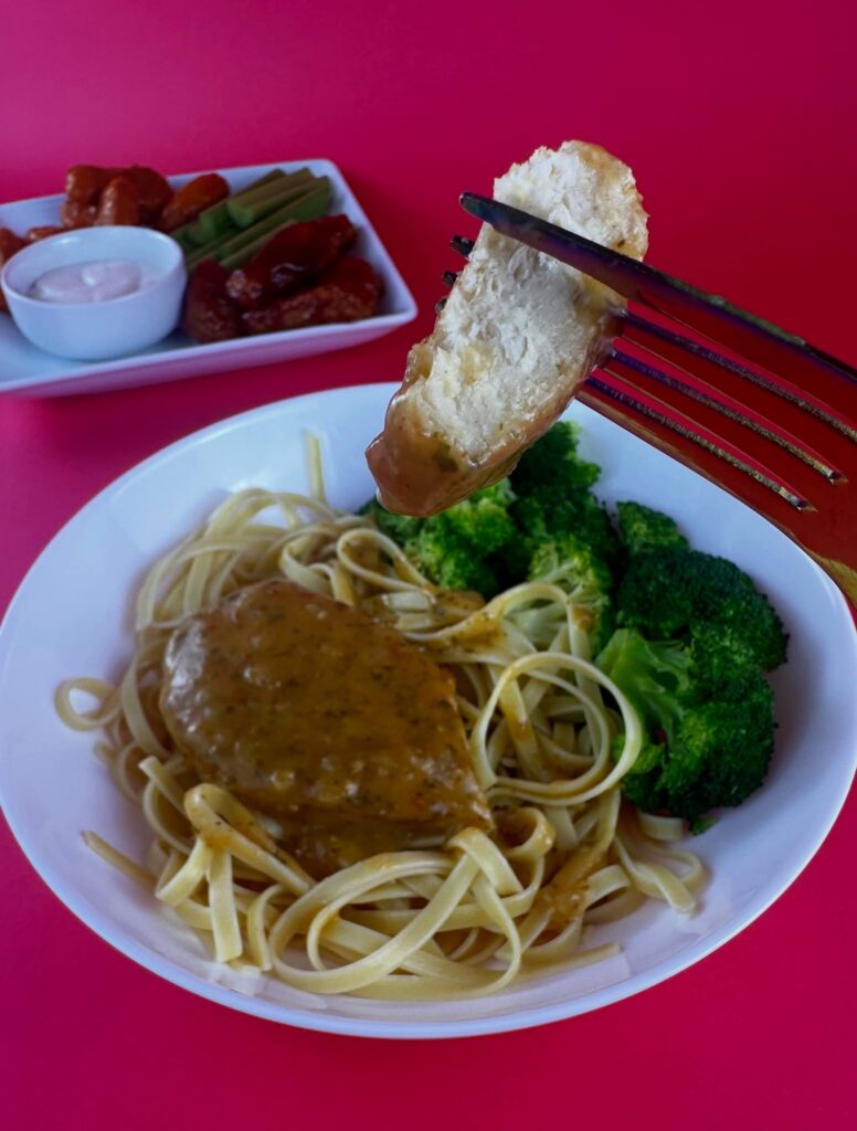 Fork holding a bite of MorningStar Farms Chik'n Breast above linguine pasta with broccoli and garlic herb sauce.