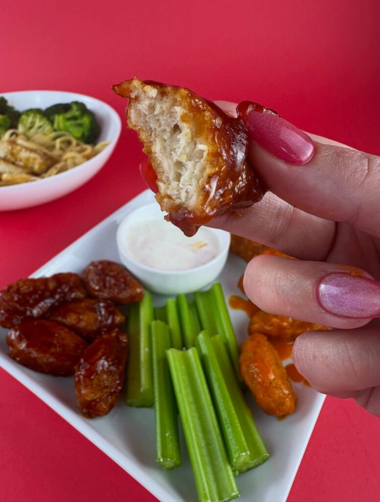 Hand holding a bitten MorningStar Farms BBQ Chik'n Wing showing the tender plant-based texture.