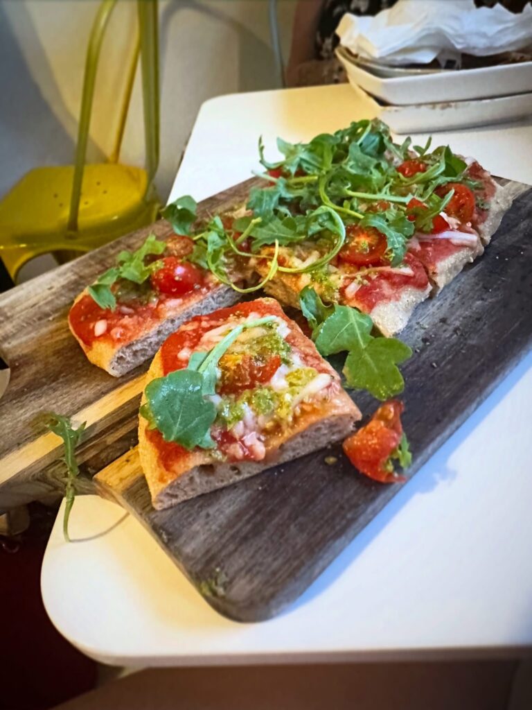 Vegan Margarita Flatbread made with local sourdough, vegan mozzarella, cherry tomatoes, arugula, lemon zest, and dairy-free pesto.