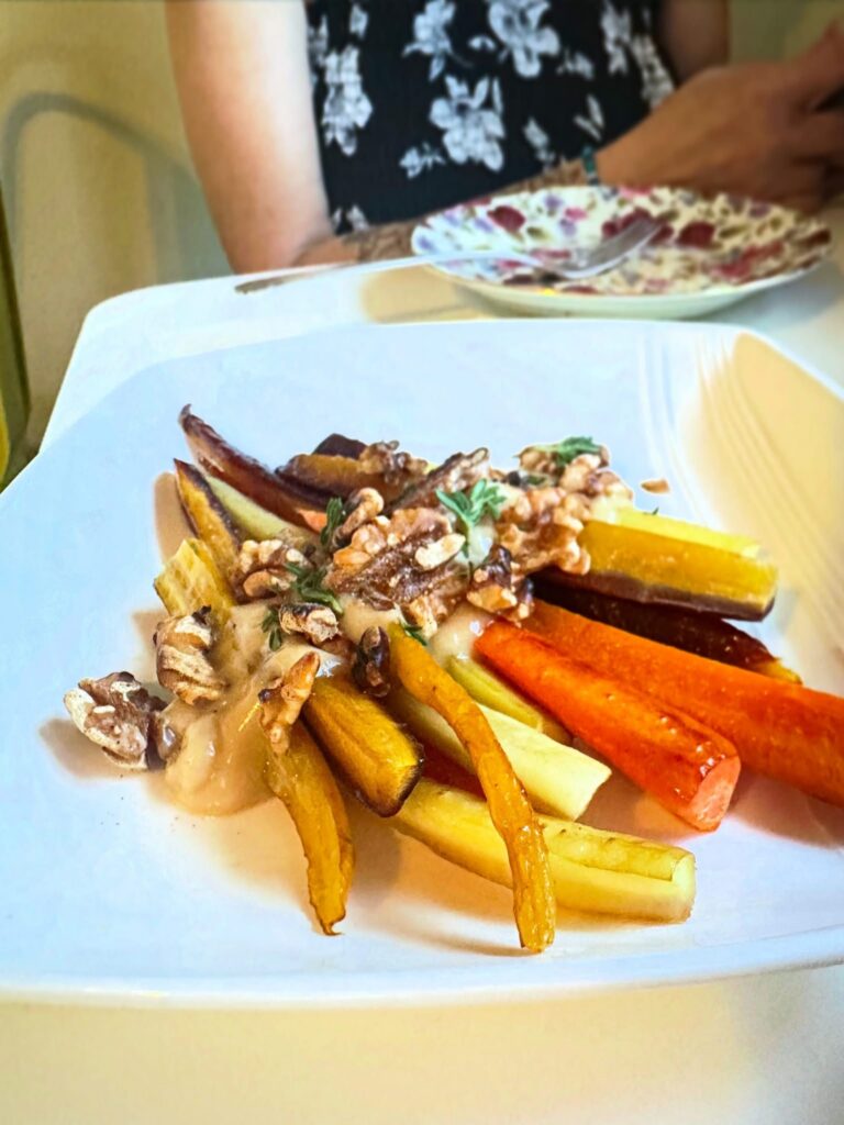 Roasted rainbow carrots topped with vegan yogurt, mushrooms, walnuts, rosemary, and paprika at Alchemist Café.