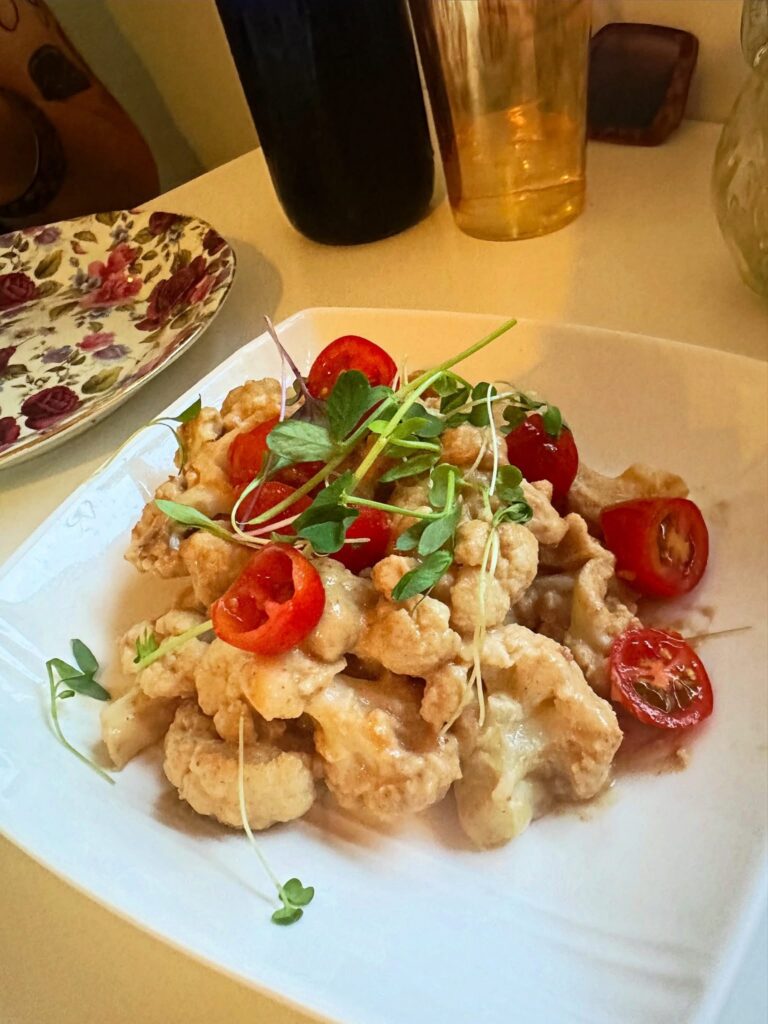 Vegan cauliflower bites topped with microgreens and cherry tomatoes, served with a savory sauce at Alchemist Café.