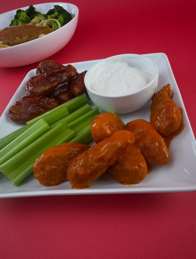 MorningStar Farms Buffalo and BBQ Chik'n Wings served with celery sticks, vegan ranch, and pasta in the background.