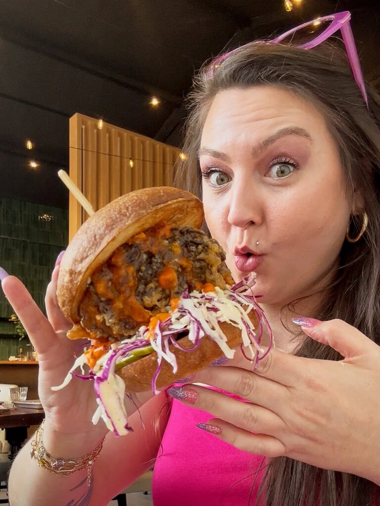 Your Neighborhood Vegan holding a large Buffalo Blue fried mushroom sandwich at Fungi Foods in Oakland.