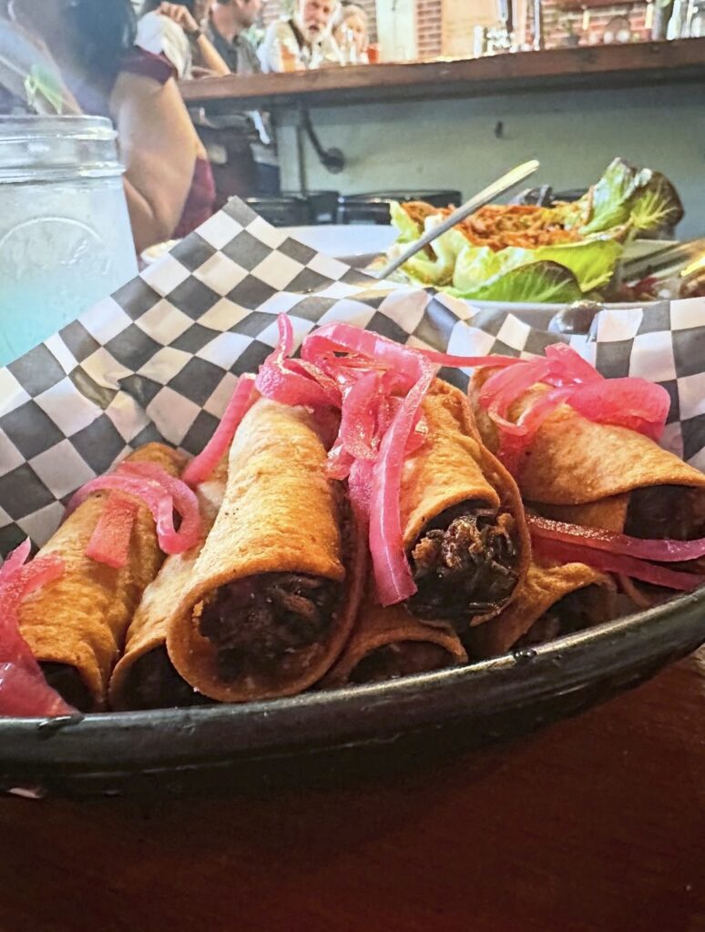 Crispy jackfruit carnitas taquitos with pickled onions served family-style at Cast Iron Trading Co.