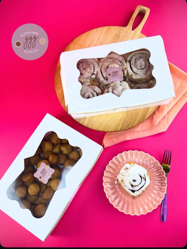 Gluten Gone Goodies vegan cinnamon rolls and donut holes displayed in bakery boxes with pink tableware.