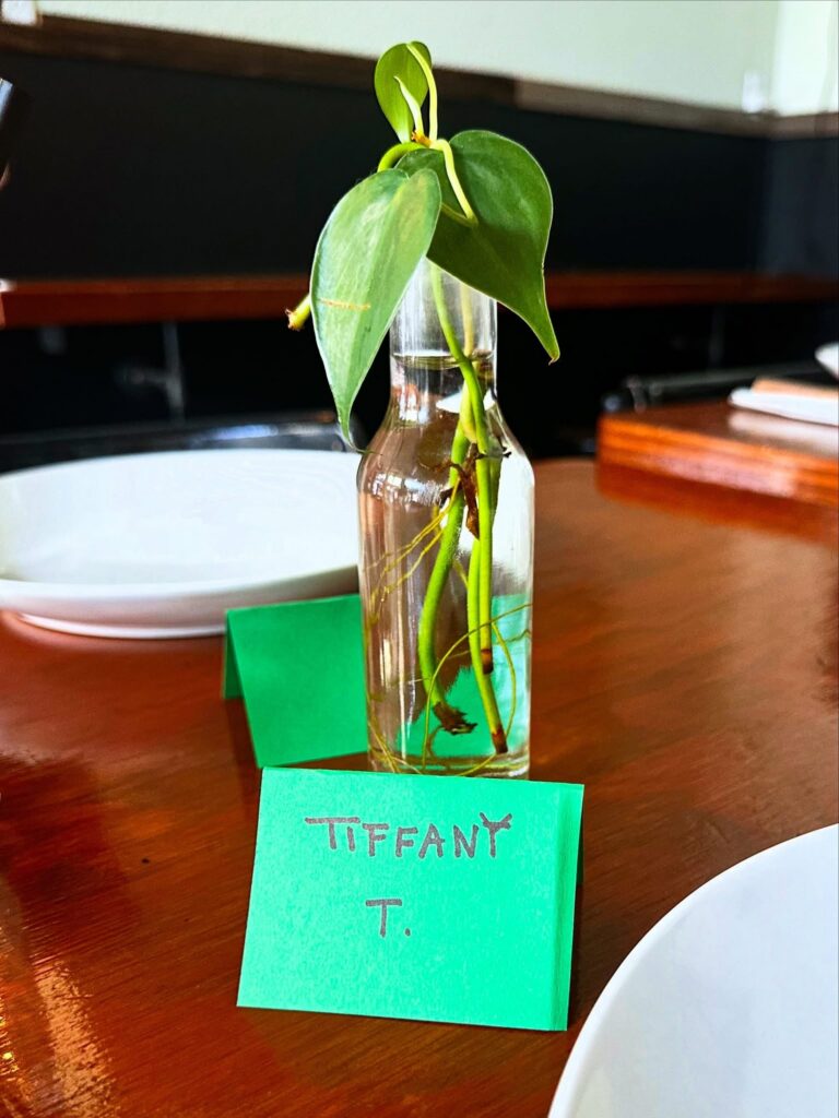 Place setting with a handwritten name card and a philodendron cutting centerpiece at Cast Iron Trading Co.'s Vegan Roast dinner in Stockton.