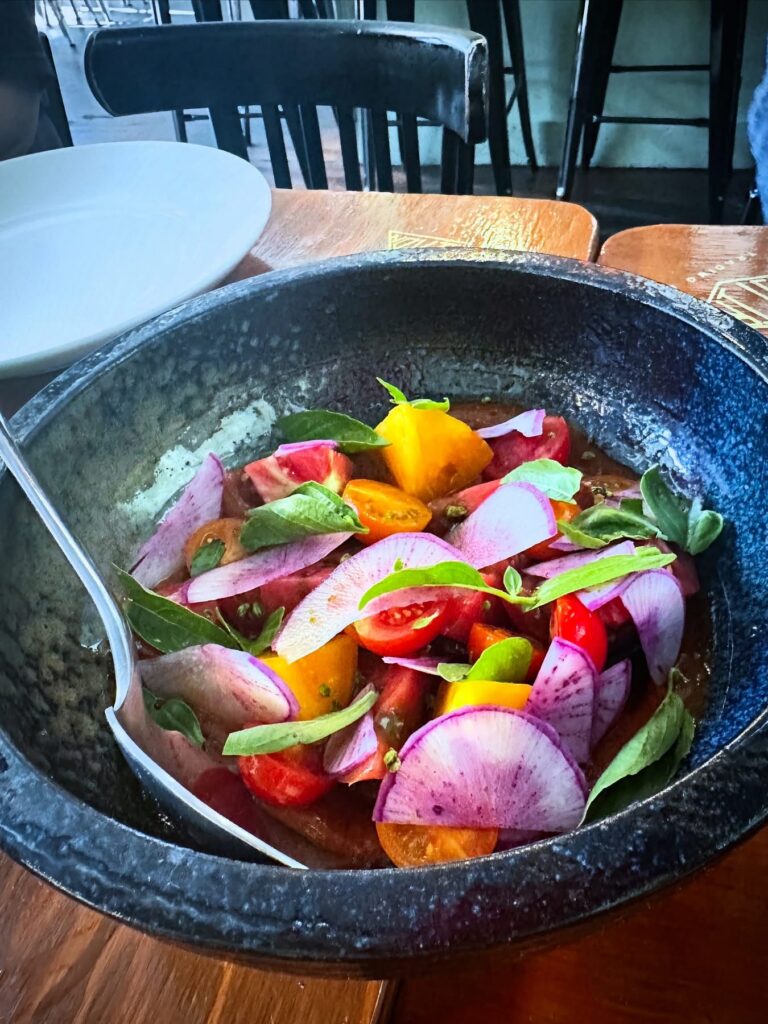 Heirloom tomato salad with peach chamoy, shaved purple daikon, cherry tomatoes, and fresh basil served during Vegan Roast.