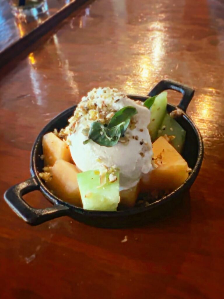 Fresh melon served with oat ice cream, seeded brittle, basil, and rosemary oil for dessert at Vegan Roast.