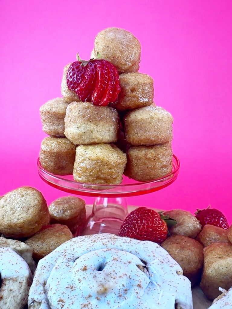 Stack of vegan gluten-free glazed donut holes topped with a strawberry beside a cinnamon roll.