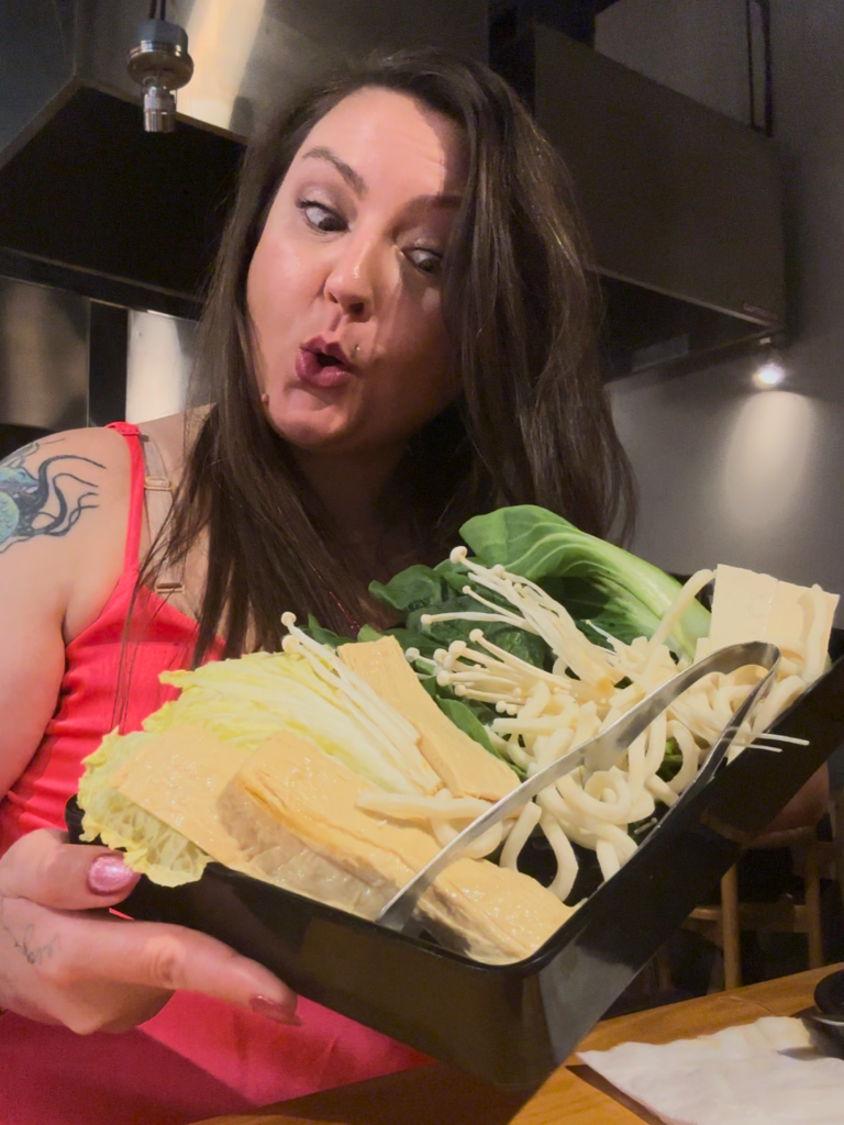 Your Neighborhood Vegan is holding the vegan vegetable platter with tofu, mushrooms, cabbage, and noodles at MUMU Hot Pot