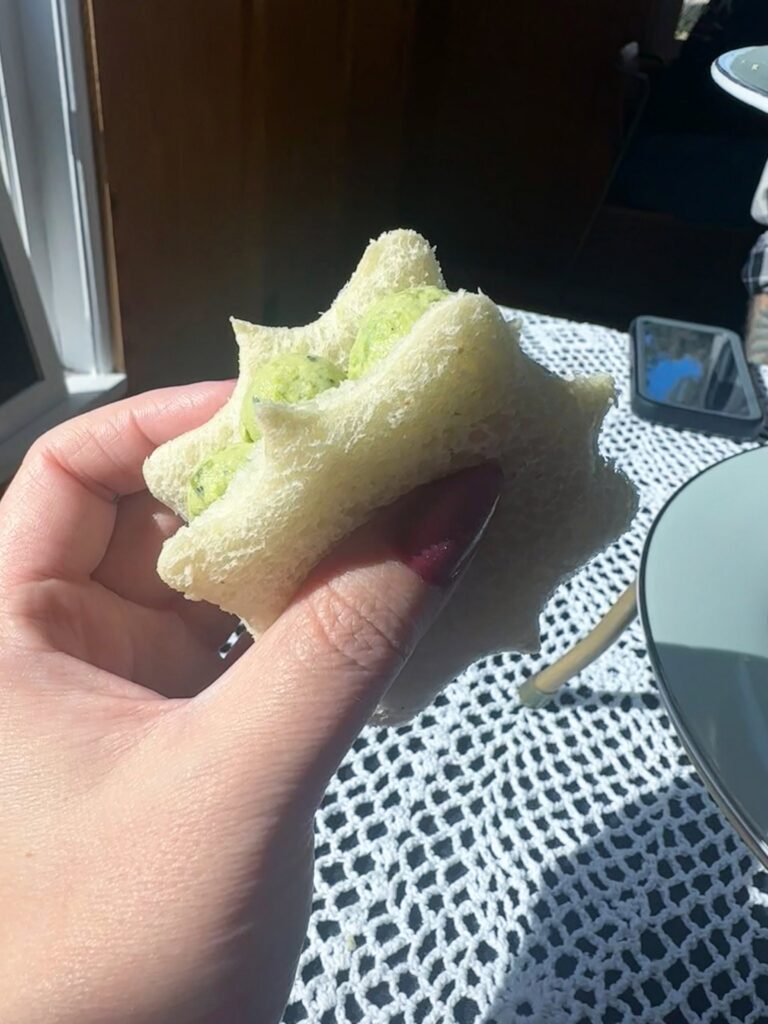 elegant-shaped vegan cucumber finger sandwich held over the tea table at Lady Bird Tea House.