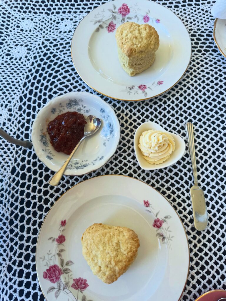 Two heart-shaped vegan scones served with strawberry jam and dairy-free clotted cream on a lace-covered tea table