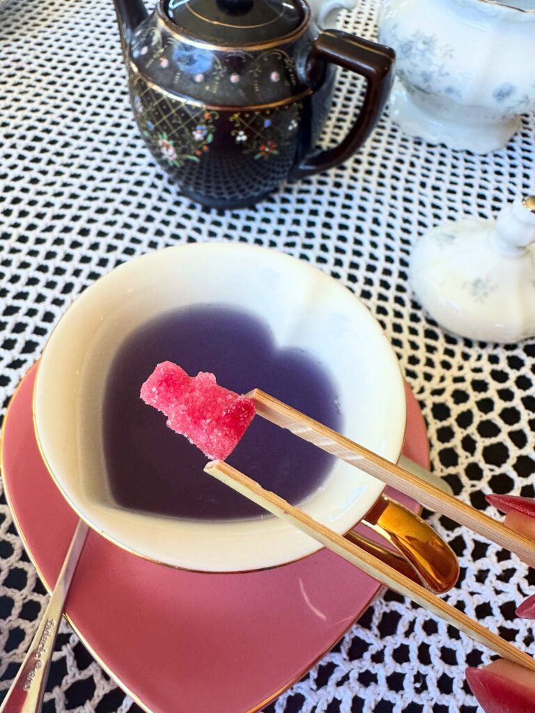 Purple Punch tea changing color as pink vegan sugar is added to a heart-shaped teacup.