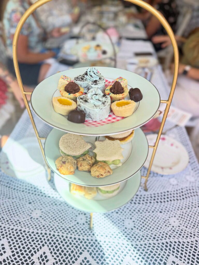 Tiered tea stand displaying Vegan Dollhouse desserts, finger sandwiches, and savory bites.