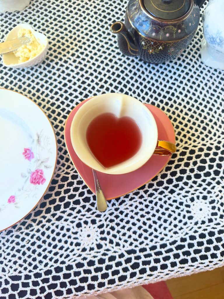 Cup of tea served in a pink heart-shaped teacup beside a floral teapot at the vegan afternoon tea.