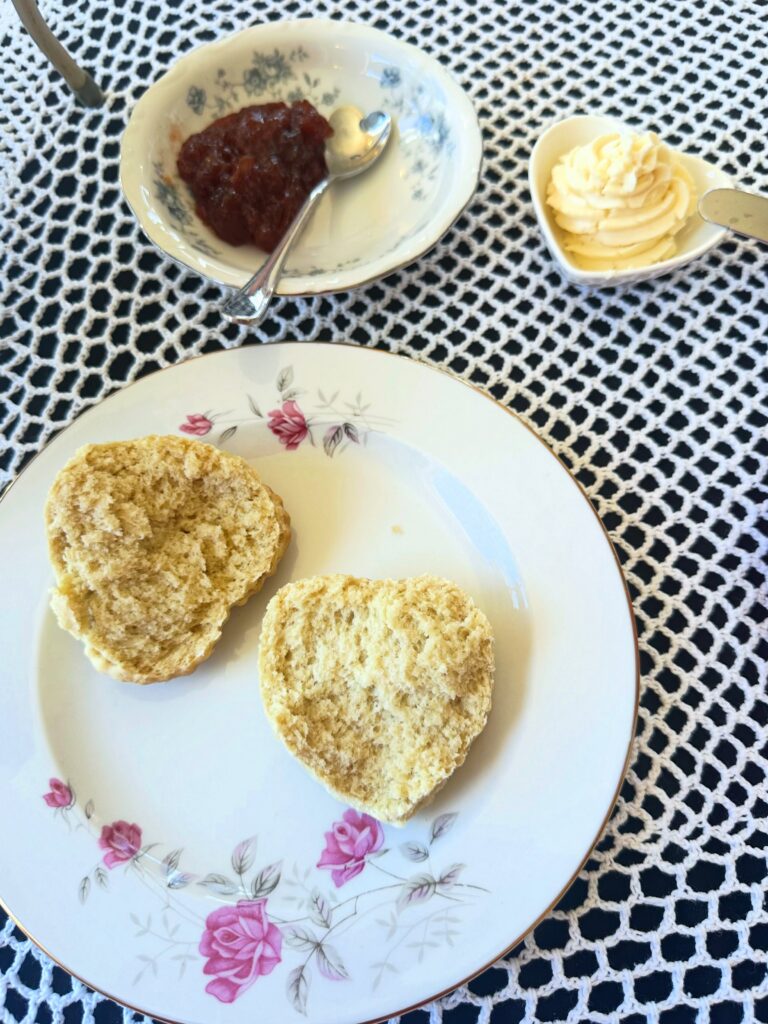 Heart-shaped vegan scone split open on a floral plate with strawberry jam and dairy-free clotted cream.