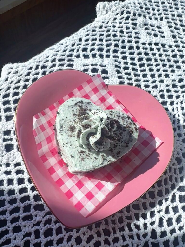 Heart-shaped slice of vegan mint cookies and cream cake on a pink plate.