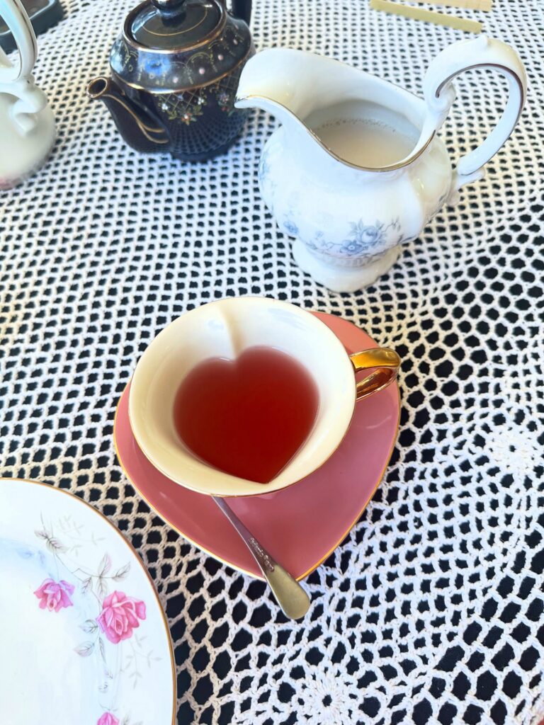 Pink tea in a pink heart-shaped teacup beside a floral teapot and dairy-free creamer.