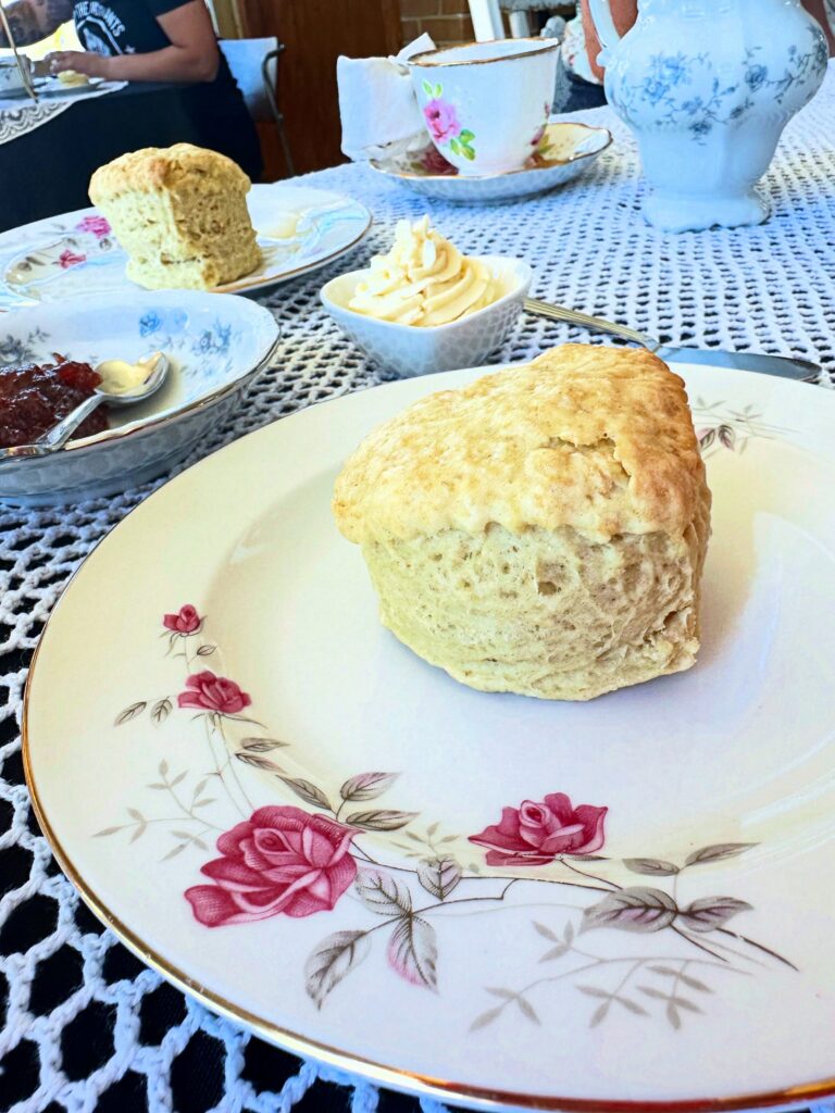 Heart-shaped vegan British scone served on a vintage floral plate with strawberry jam and dairy-free clotted cream.