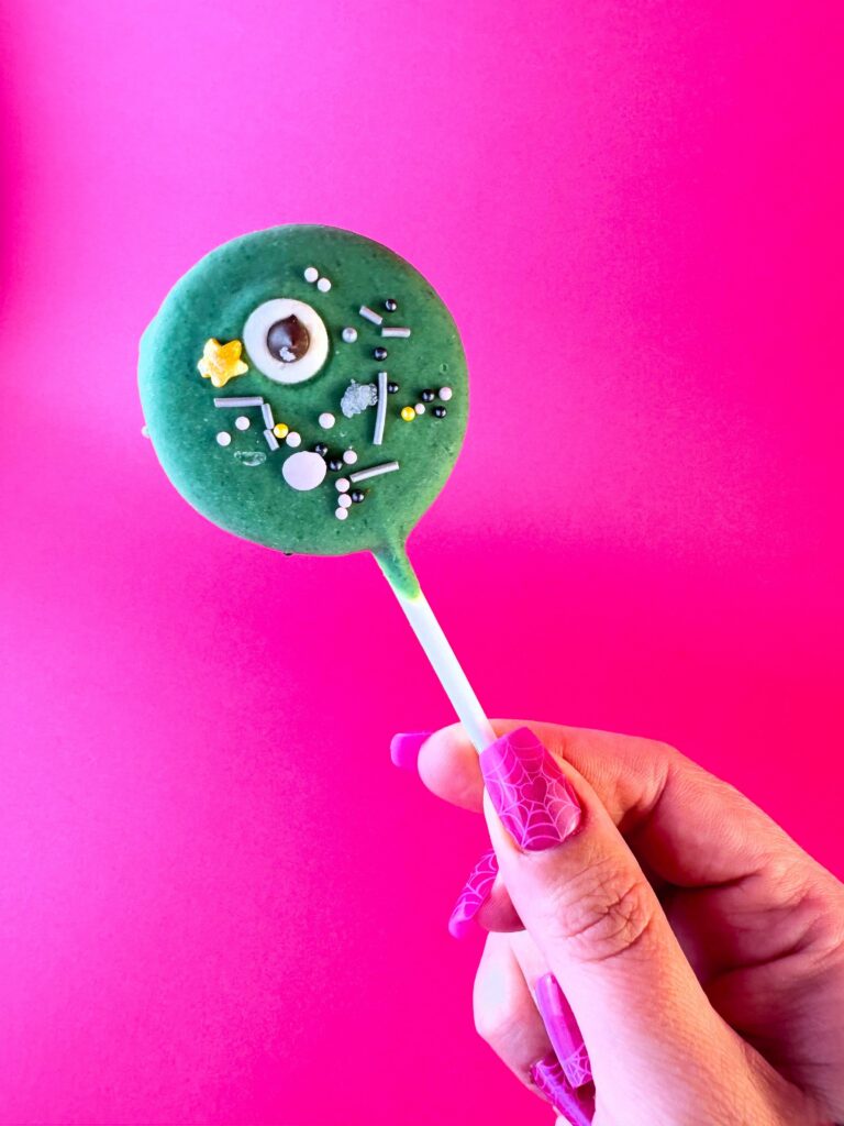 Green Monster Cookie Pop from Vegan Dollhouse decorated with a candy eye and Halloween sprinkles.