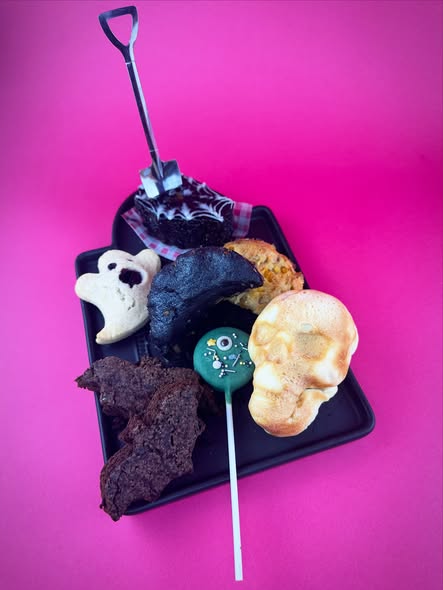 Assortment of Vegan Dollhouse Halloween treats photographed on a black tray against a pink background.
