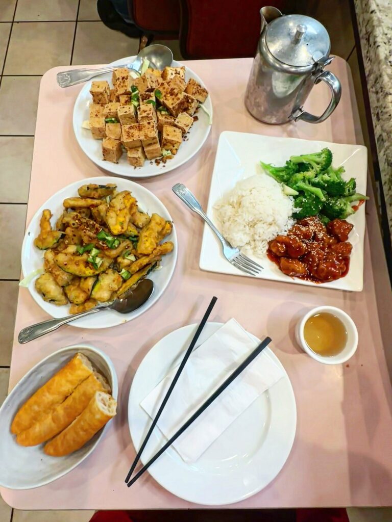 Table filled with vegan Chinese food at Veggie Lee including salt and pepper tofu, pumpkin, sesame chicken, broccoli, rice, and Chinese donuts